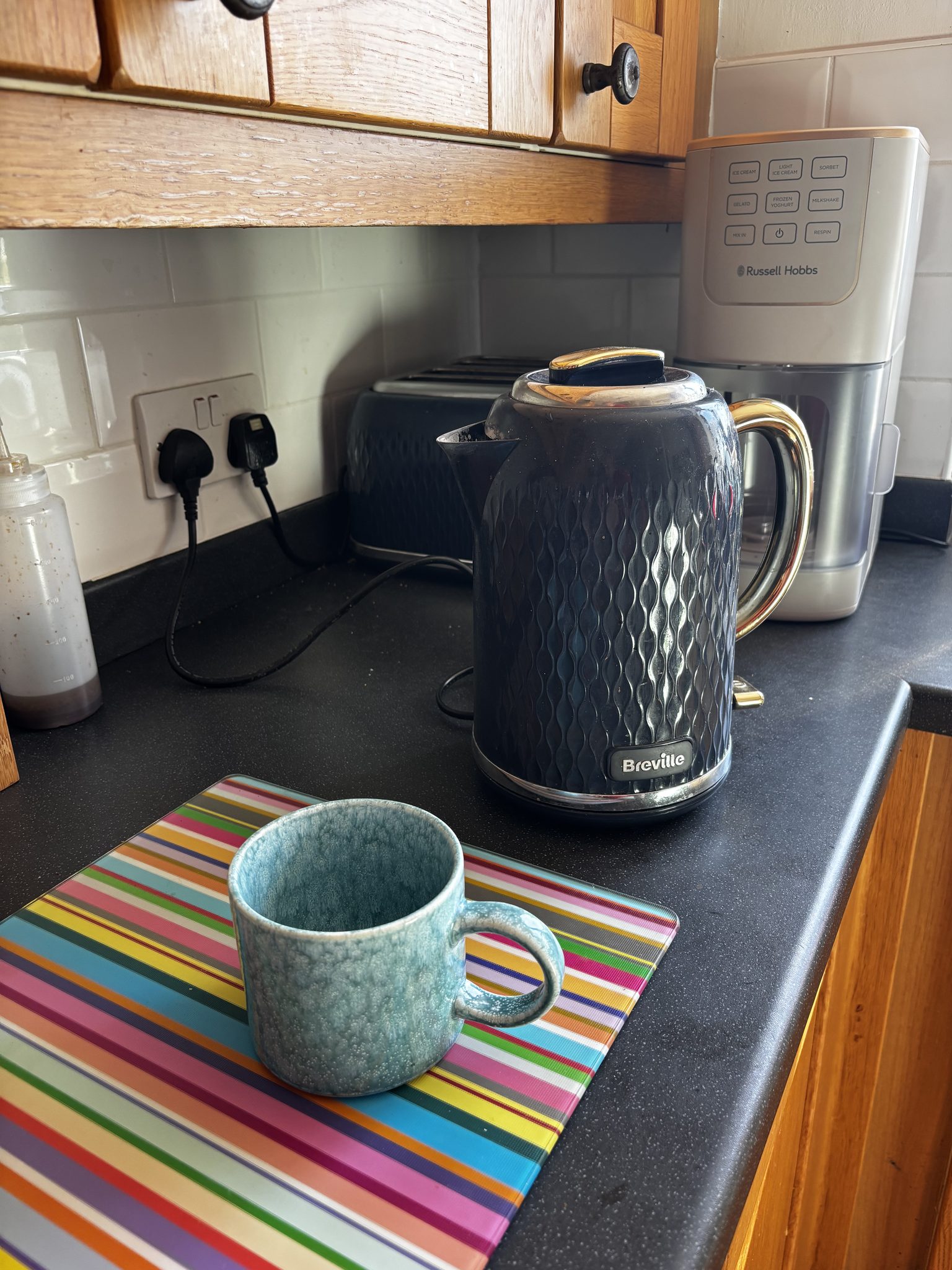 A navy Breville kettle beside an empty stoneware mug on a striped worktop saver