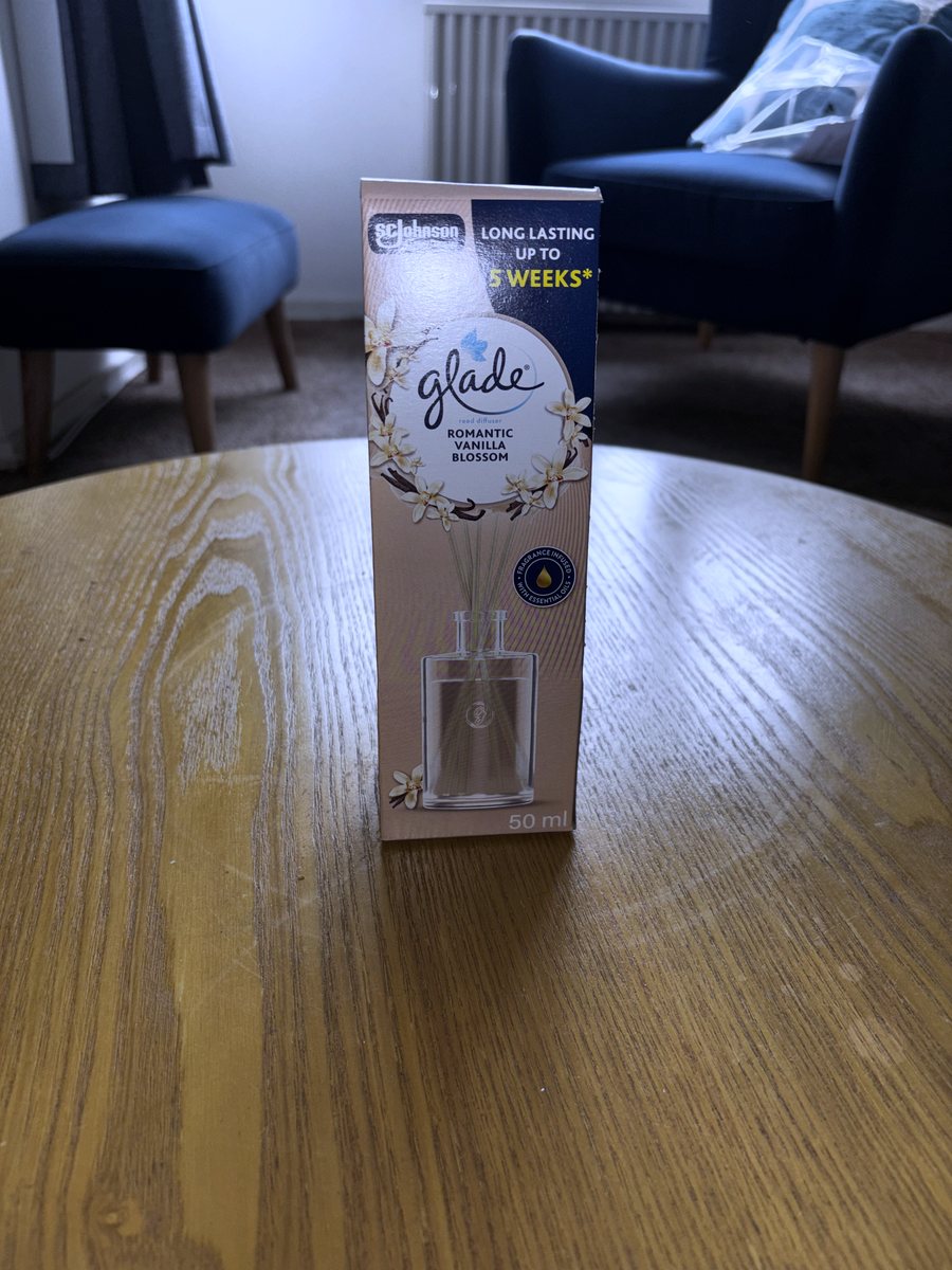 The Glade Romantic Vanilla Blossom reed diffuser in its box on a wooden table, the box front reading long lasting up to 5 weeks