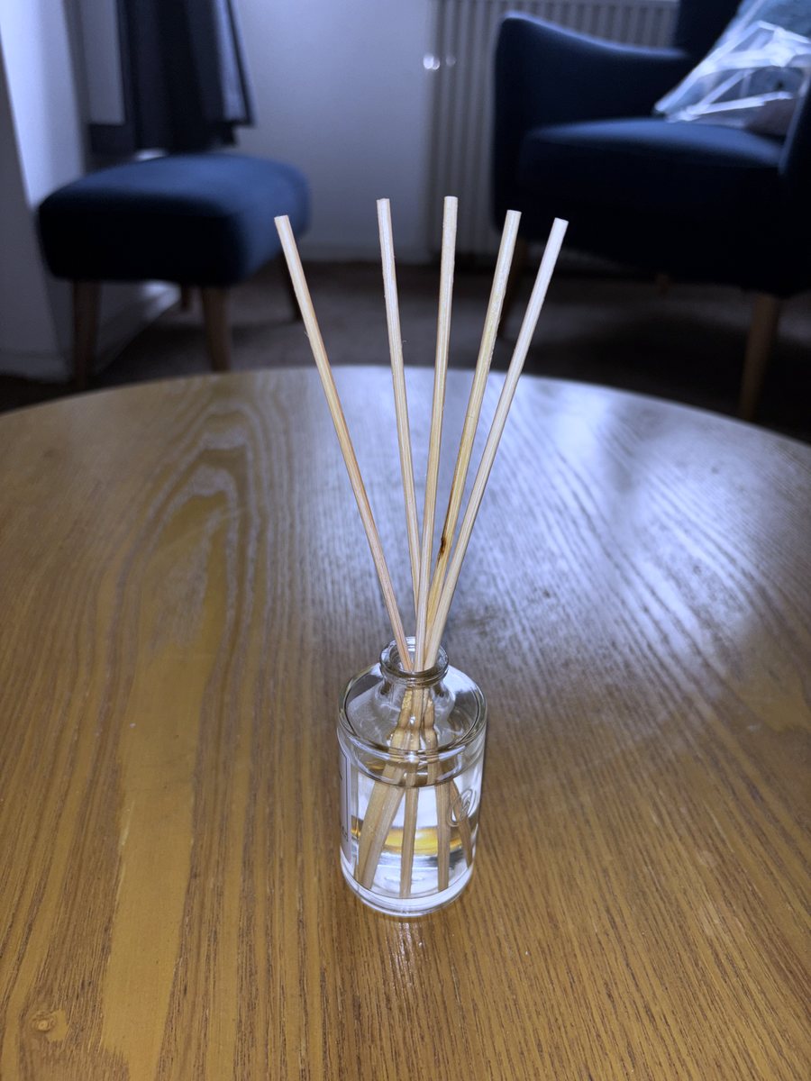 The Glade Romantic Vanilla Blossom reed diffuser set up with its reeds in, on a wooden table in a living room