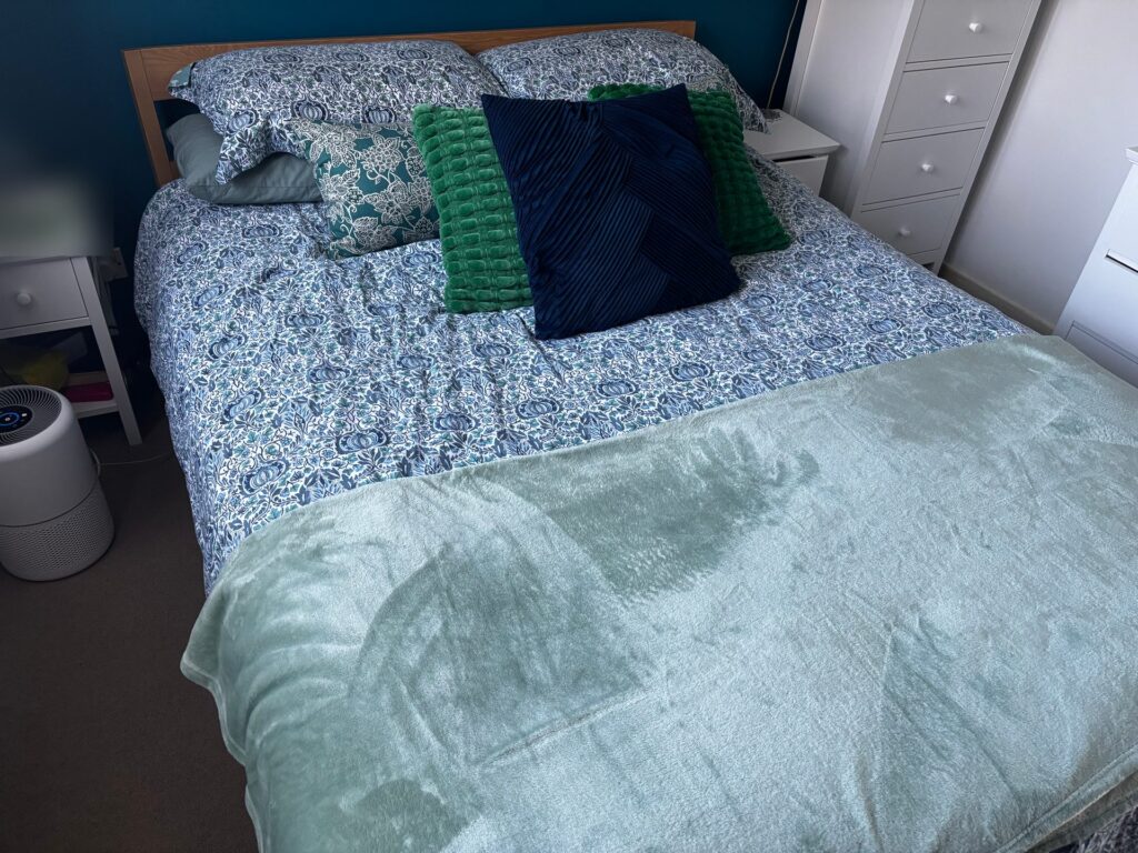 A king-size bed made up for winter: blue floral duvet, green and navy cushions and a mint fleece blanket