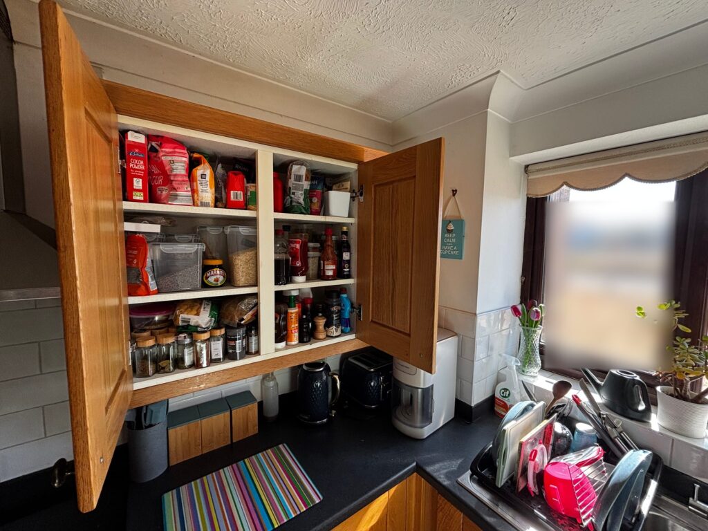 A UK kitchen with the store cupboard doors open and the window and sink beyond