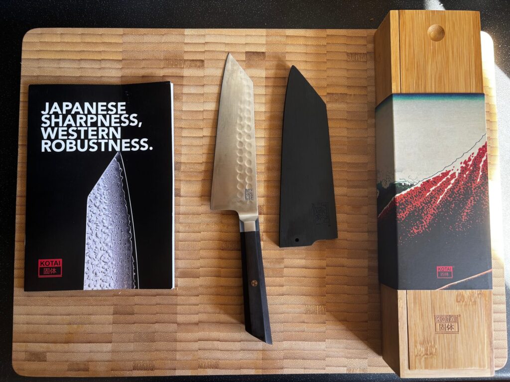 A Kotai bunka knife with its black sheath, booklet and bamboo box laid out on a bamboo chopping board