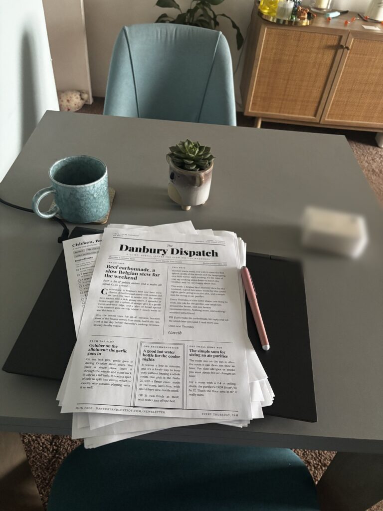 A printed copy of the Danbury Dispatch on a table at home, beside a mug and a small succulent